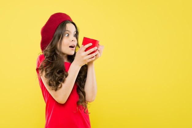 Ragazza felice con capelli ricci lunghi in berretto. infanzia. salone di parrucchiere. bambino parigino su sfondo giallo. bellezza e moda. bambina in cappello stile francese. L'ora del tè. concetto di stile di vita. copia spazio.