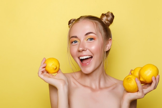 Ragazza felice con i limoni su una parete gialla