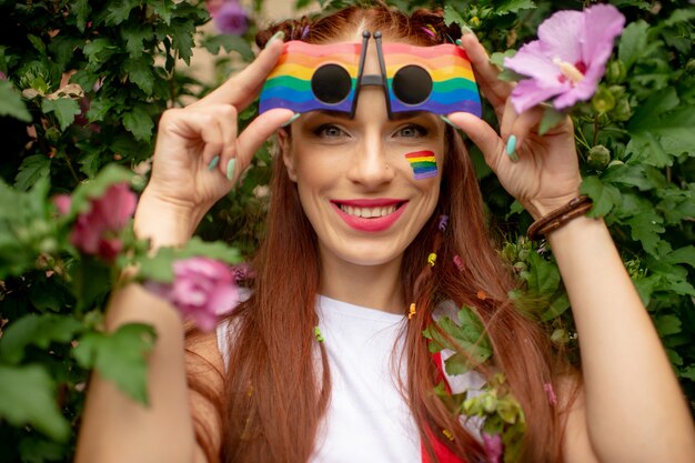 Ragazza felice con la bandiera del lgbt sul suo fronte che indossa i vetri dell'arcobaleno e che posa con il fronte sorridente