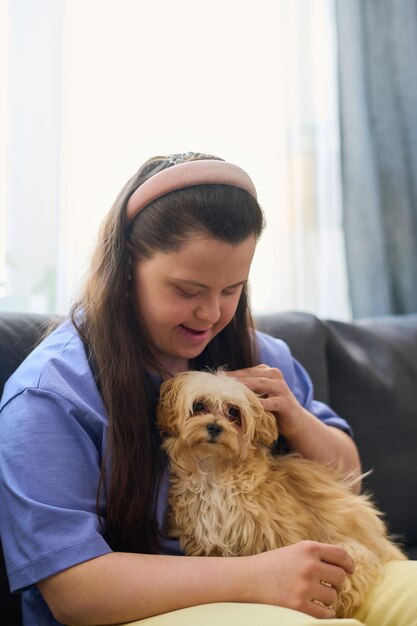 Ragazza felice con la sindrome di down che coccola un cane lanuginoso seduto sulle sue ginocchia