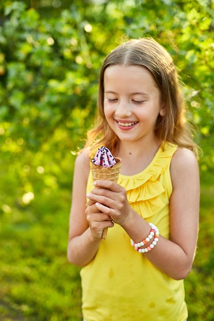 Ragazza felice con le parentesi graffe che mangia il cono gelato italiano che sorride mentre riposa nel parco il giorno d'estate