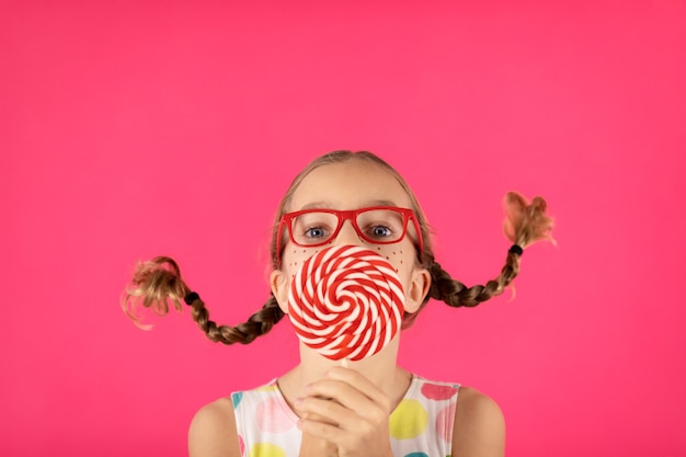 Ragazza felice con lecca-lecca contro il muro rosa.