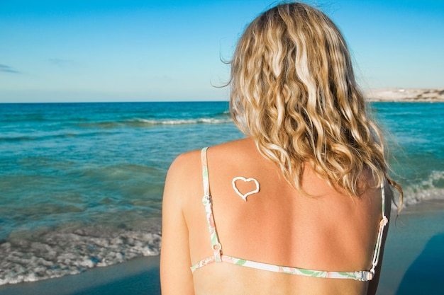 Ragazza felice con un cuore sulla schiena in riva al mare all'aperto