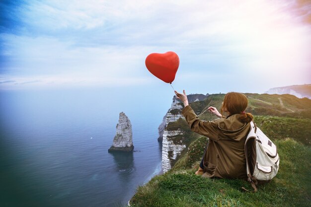 Ragazza felice con un palloncino rosso a forma di cuore sullo sfondo del paesaggio Etretat. Francia