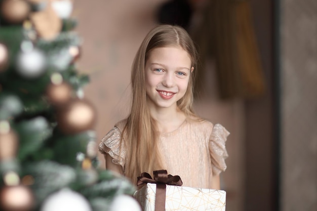 Ragazza felice con un regalo di Natale in piedi vicino all'albero di Natale