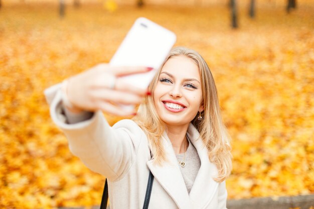 Ragazza felice con un sorriso che fa selfie in una giornata autunnale di fogliame giallo