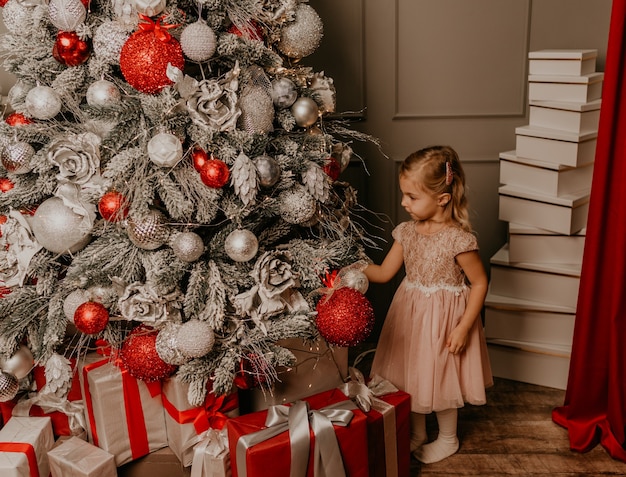 Ragazza felice dei bambini che celebra il nuovo anno e il Natale all'albero di Natale decorato e alle ghirlande