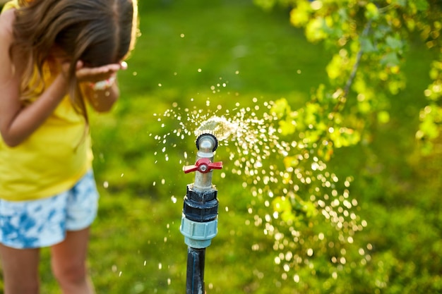 Ragazza felice del bambino che gioca a mano con l'irrigatore del giardino