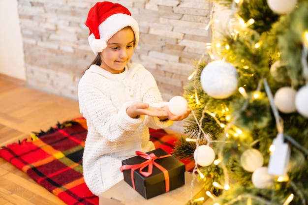 Ragazza felice del bambino che ride nella stanza sopra l'albero di Natale. Indossa un maglione alla moda. Infanzia. Periodo natalizio.