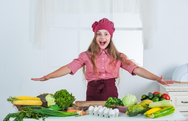 Ragazza felice del bambino in cappello del cuoco e grembiule nella salute della cucina