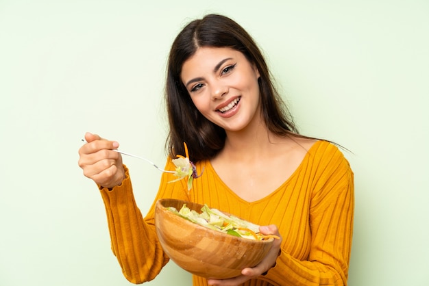 Ragazza felice dell&#39;adolescente con insalata sopra la parete verde