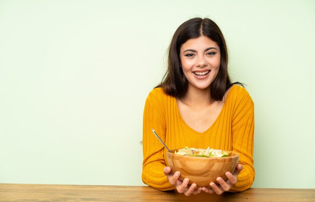 Ragazza felice dell'adolescente con insalata sopra la parete verde