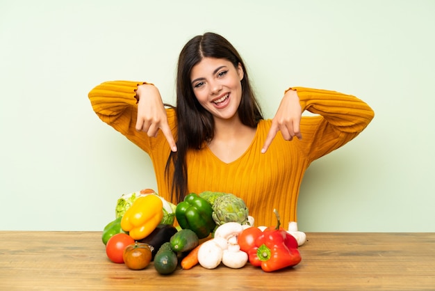 Ragazza felice dell'adolescente con molte verdure sopra la parete verde