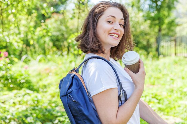 Ragazza felice dell'allievo positivo con lo zaino che sorride sulla priorità bassa verde del parco.