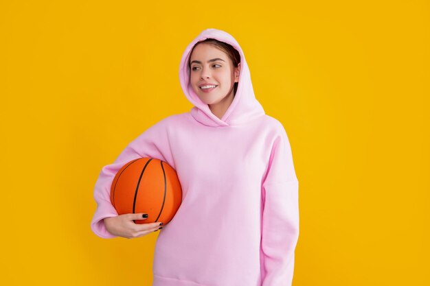 Ragazza felice dello studente hipster con palla da basket su sfondo giallo