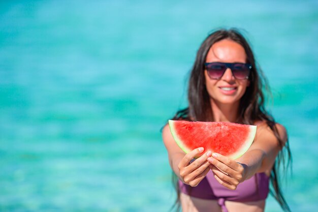 Ragazza felice divertendosi sulla spiaggia e mangiando anguria