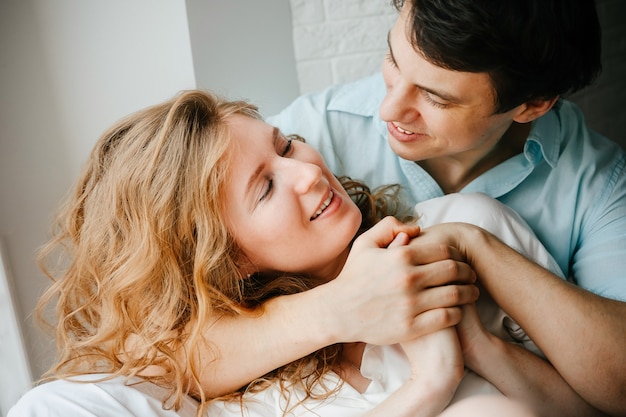 Ragazza felice e uomo che si abbracciano vicino alla finestra in casa. Vestiti bianchi e blu. San Valentino.