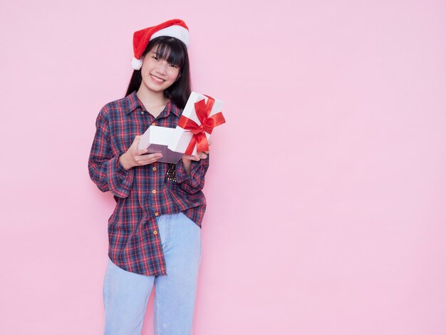 Ragazza felice in cappello della Santa che apre una confezione regalo contro il muro rosa