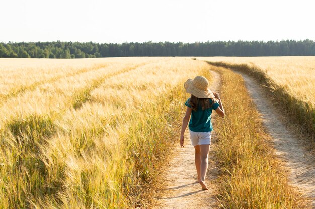 ragazza felice in cappello di paglia andare a piedi nudi sul sentiero nel campo agricolo