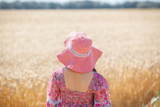 Ragazza felice in cappello sul campo di grano. Cappello grande e capelli lunghi