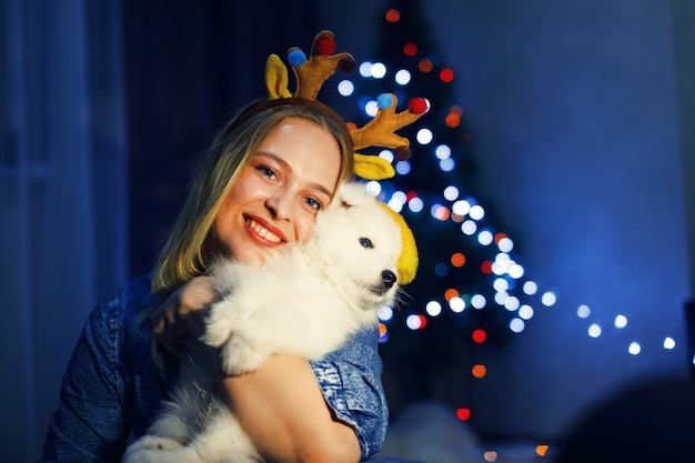 Ragazza felice in corna con cane husky samoiedo in decorazioni natalizie