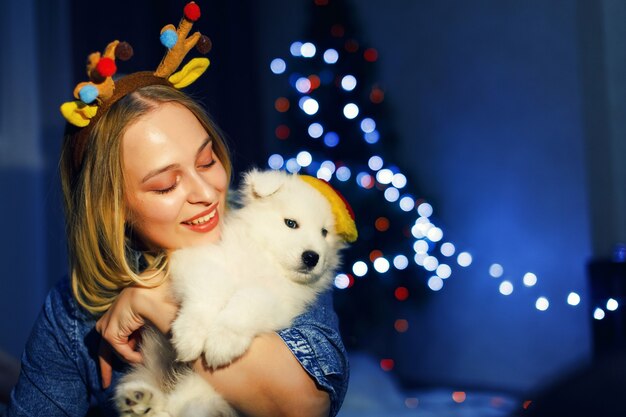 Ragazza felice in corna con cane husky samoiedo in decorazioni natalizie