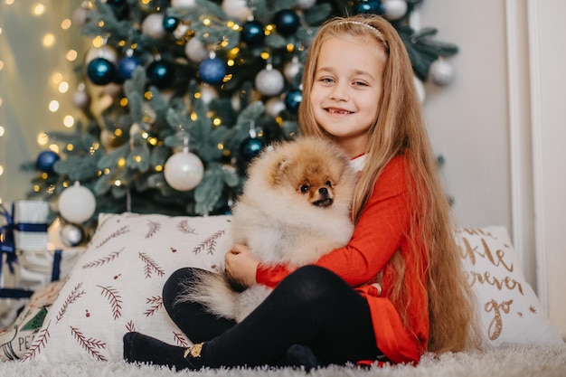 Ragazza felice in posa con un cucciolo carino, albero di Natale sullo sfondo, regalo soffice tanto atteso, gioia