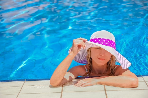 Ragazza felice in un cappello a bordo piscina sulla natura della riva del mare