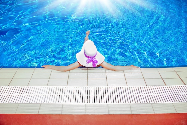 Ragazza felice in un cappello a bordo piscina sulla natura della riva del mare