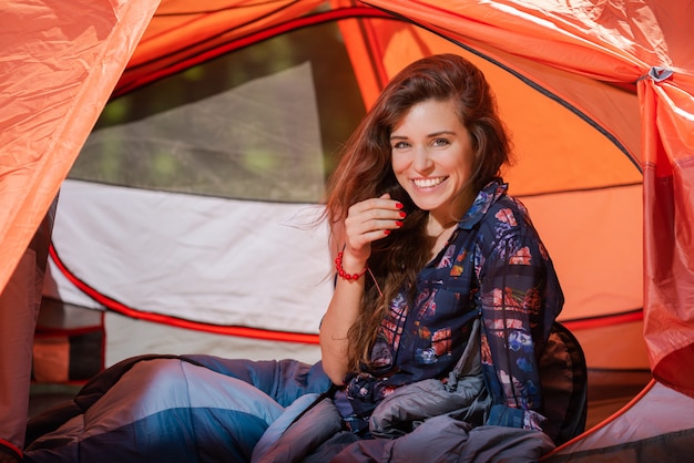 Ragazza felice in un sacco a pelo dentro una tenda