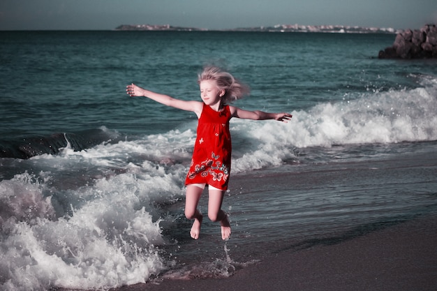 Ragazza felice in vestito colorato che salta sulle onde sulla spiaggia