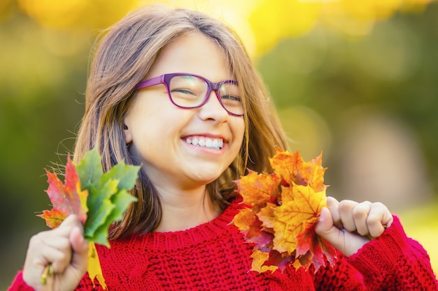 Ragazza felice sorridente e gioiosa che tiene le foglie autunnali Ragazza con foglie d'acero in cardigan rosso