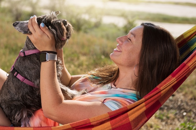 Ragazza felice su un picnic sdraiato su un'amaca che tiene un piccolo cane tra le braccia, stile di vita, concetto