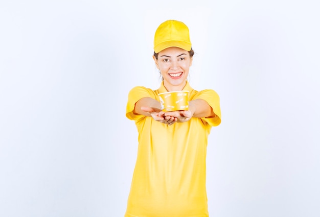 Ragazza femminile in uniforme gialla che consegna una tazza di noodle da asporto gialla al cliente.