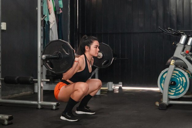 Ragazza fitness con pantaloncini arancioni che fa squat con bilanciere in palestra