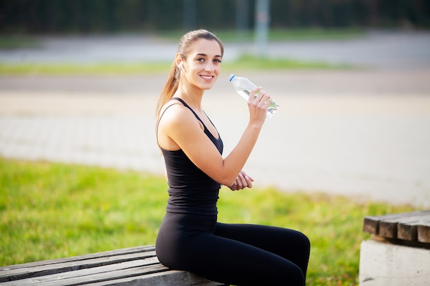 Ragazza fitness. Giovane bella donna in acqua potabile degli abiti sportivi in parco