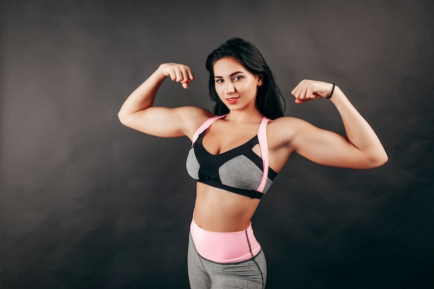 Ragazza forte fitness mostra muscoli in studio