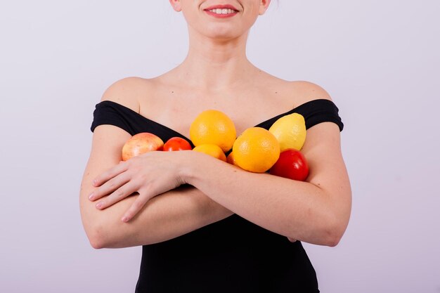 Ragazza fresca sorridente con gli occhiali da sole in costume da bagno nero che posa con frutta e ride