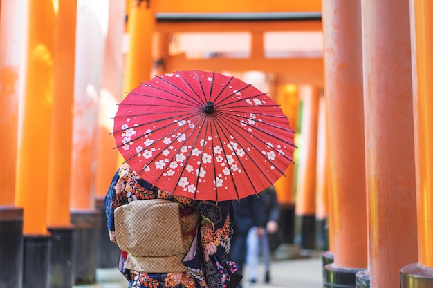 Ragazza geishe che indossa un kimono giapponese tra Tori Gate in legno rosso