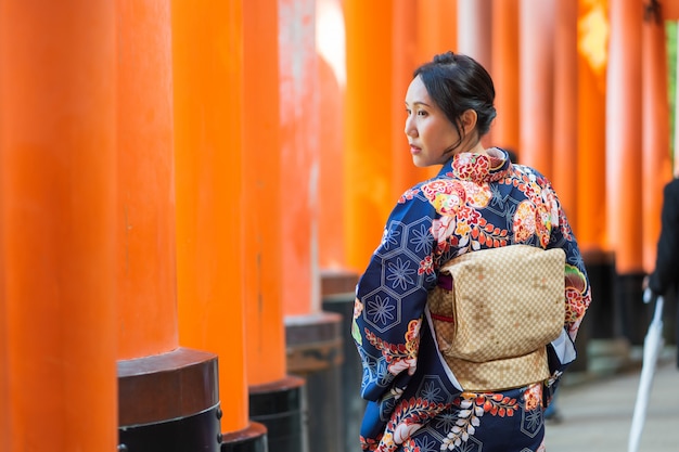 Ragazza geishe che indossa un kimono giapponese tra Tori Gate in legno rosso