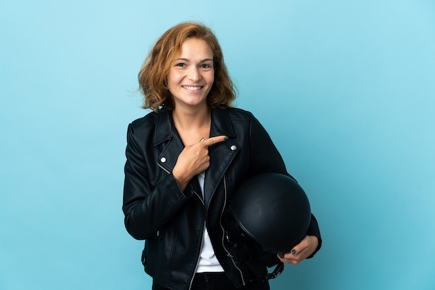 Ragazza georgiana che tiene un casco del motociclo isolato su priorità bassa blu che indica al lato per presentare un prodotto