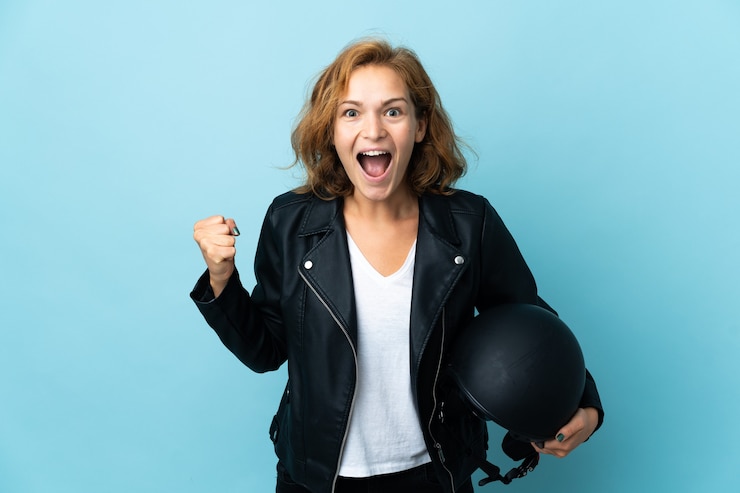 Foto ragazza georgiana che tiene un casco del motociclo isolato sull'azzurro che celebra una vittoria nella posizione del vincitore