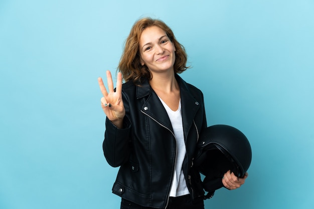 Ragazza georgiana che tiene un casco del motociclo isolato sull'azzurro felice e contando tre con le dita