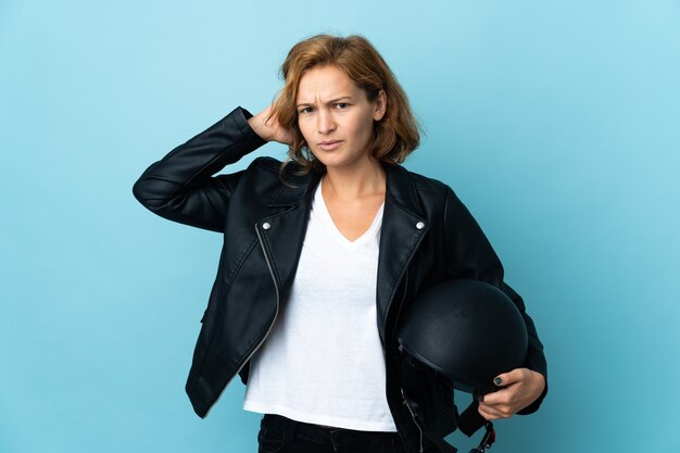 Ragazza georgiana che tiene un casco del motociclo isolato sulla parete blu che ha dubbi