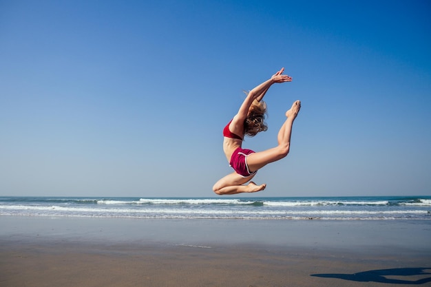 Ragazza ginnasta che fa spacca grand jette nell'aria Bella giovane donna ginnasta in forma che lavora fuori l'elemento di ginnastica artistica dell'esecuzione che salta facendo il salto diviso ballando sulla spiaggia del mattino d'estate