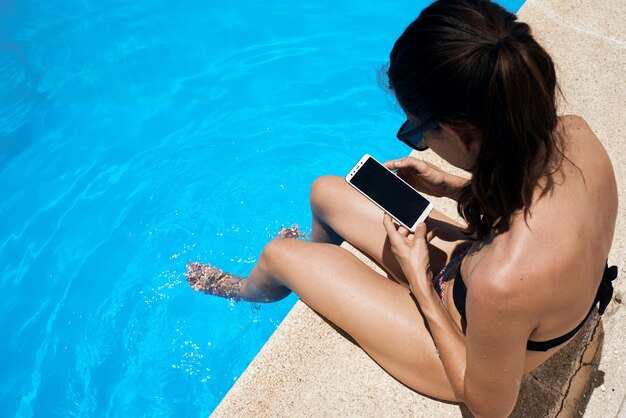 Ragazza giovane a prendere il sole in piscina utilizzando il suo telefono cellulare