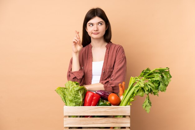 Ragazza giovane agricoltore con verdure appena raccolte in una scatola con dita che attraversano e desiderano il meglio