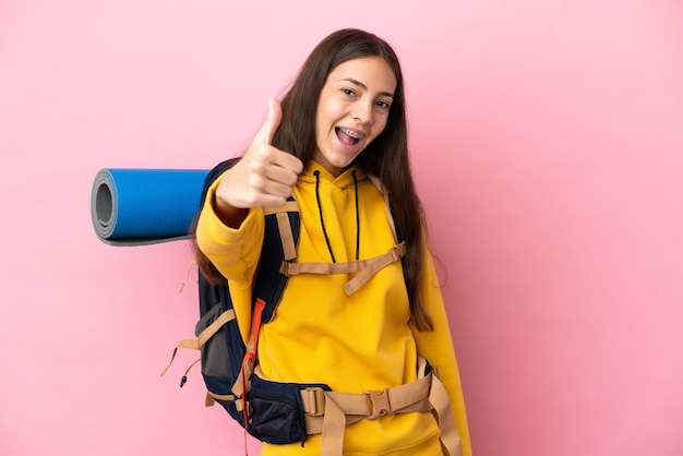 Ragazza giovane alpinista con un grande zaino isolato su sfondo rosa con i pollici in su perché è successo qualcosa di buono