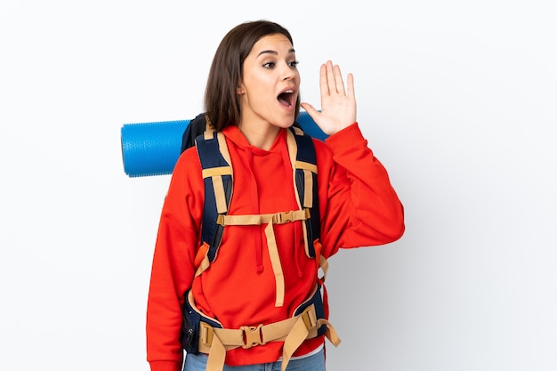 Ragazza giovane alpinista con un grande zaino isolato sul muro bianco che grida con la bocca spalancata