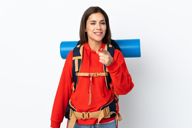 Ragazza giovane alpinista con un grande zaino isolato sul muro bianco punta il dito contro di te